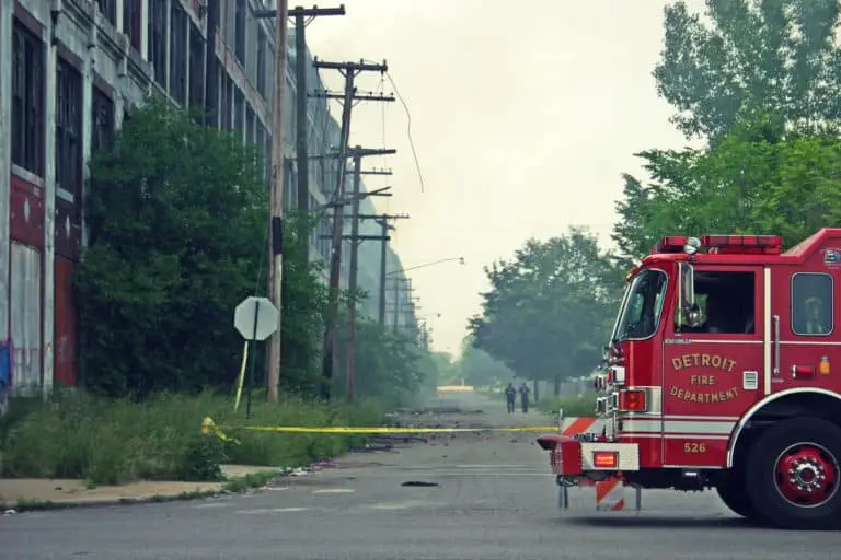 A fire engine from the detroit fire department parked on a deserted street, cordoned off with yellow caution tape, with a dilapidated building in the background, suggesting a scene of emergency response in an urban setting.